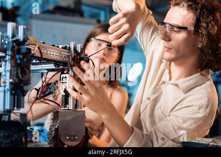 Giovane uomo e donna in occhiali protettivi che fanno esperimenti di robotica in laboratorio. Robot sul tavolo Foto Stock