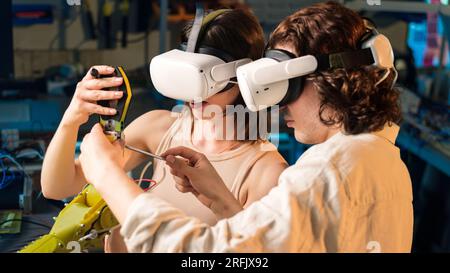 Giovane uomo e donna in occhiali VR che fa esperimenti di robotica in laboratorio. Robot sul tavolo Foto Stock