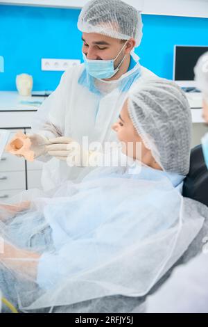 Il dentista maschio comunica con una paziente femminile in clinica Foto Stock