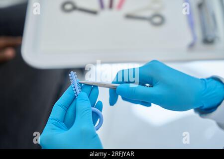 Primo piano dentista altamente qualificato che utilizza una piccola fascia di gomma che distribuisce le forze occlusali per raddrizzare i denti dei clienti in bretelle, dentistr estetico Foto Stock