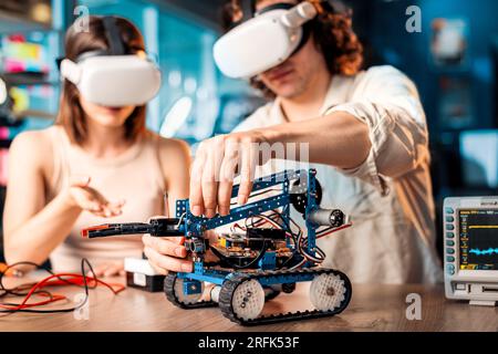 Giovane uomo e donna in occhiali VR che fa esperimenti di robotica in laboratorio. Robot e strumenti sul tavolo Foto Stock