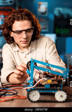 Giovane uomo con occhiali protettivi che fa esperimenti di robotica in laboratorio usando strumenti speciali Foto Stock