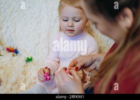 la madre sta colorando le unghie della sua bambina con uno smalto rosa. Divertirsi a fare manicure a casa Foto Stock