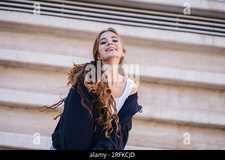 Simpatica ragazza sorridente e guardante la fotocamera accanto a Un muro di cemento. Foto Stock