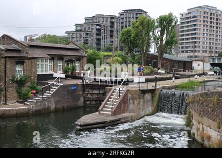 Vista della chiusa di St Pancras 4 sul Regent's Canal con le porte delle chiuse, l'acqua che cade sulla diga e alti blocchi di appartamenti sullo sfondo. Foto Stock