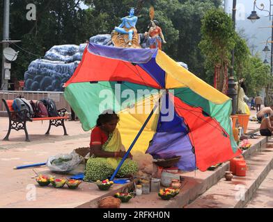 Una povera donna che vende oggetti puja a Triveni Ghat, Rishikesh, che tiene un ombrello per proteggersi dal sole. Rishikesh. Uttarakhand. India. Asia. Foto Stock