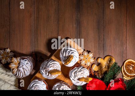 Cupcake di pan di zenzero di Natale. Cupcake al cioccolato dolce e muffin bianchi con panna montata, spezie invernali e biscotti al pan di zenzero, decorazioni in legno c Foto Stock