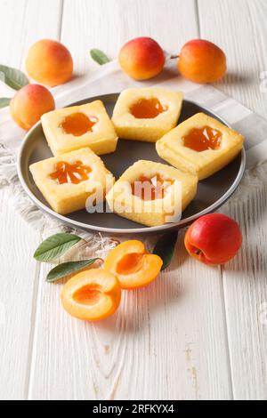 Biscotti morbidi quadrati con marmellata di albicocche da vicino su un piatto sul tavolo. Verticale Foto Stock