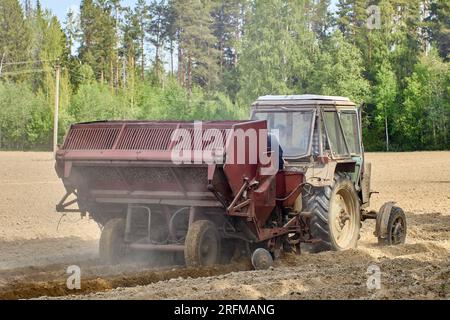 Un trattore agricolo a ruote con piantatrice di patate agganciata sta piantando patate in un campo agricolo durante la semina. Foto Stock