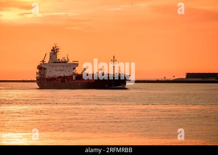 Tramonto estivo arancione su una petroliera che entra in un porto marittimo Foto Stock