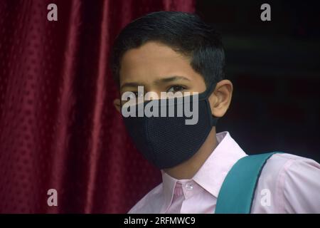 adolescente studente ragazzo che indossa l'uniforme scolastica e la maschera di faccia andando a scuola con il pacchetto borsa in pandemia di virus corona Foto Stock