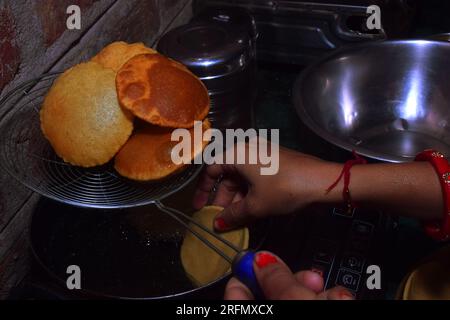 Moderna stufa nera a induzione, donna in cucina che cucina con cucchiaio, chapati fritti (puri) Foto Stock