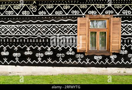 Finestra in legno sul dipinto ornamentale con motivi bianchi e neri sulle pareti in legno scuro nel vecchio villaggio slovacco di Cicmany. Patrimonio storico europeo e b Foto Stock