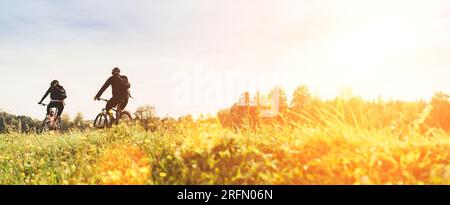 Giovane coppia uomo e donna biciclisti con zaini in sella sotto la luce del tramonto al caldo inizio autunno. Immagine del concetto di persone sportive attive Foto Stock