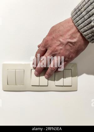 L'uomo accende la luce. La mano dell'uomo in maglione grigio preme l'interruttore della luce. Primo piano. messa a fuoco selettiva. Foto Stock