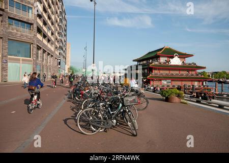 Persone che camminano e vanno in bicicletta a Oosterdokskade (sulla destra il ristorante cinese galleggiante Sea Palace), Amsterdam, Paesi Bassi Foto Stock