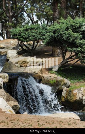 Piccola cascata che scende dai massi nella piscina d'acqua del parco pubblico. Foto Stock