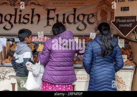 famiglia asiatica che acquista fudge da una bancarella di fudge in un mercato a cowes, sull'isola di wight, regno unito. Foto Stock