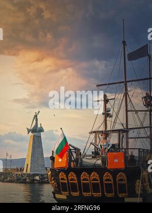 Statua di San Nicola patrono dei marinai, nella città vecchia di Nessebar, Burgas, Bulgaria. Tramonto sulla costa con una barca a vela ormeggiata Foto Stock