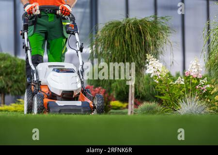 Giardini all'aperto che mantengono il lavoratore che taglia il prato da cortile utilizzando la falciatrice elettrica Foto Stock