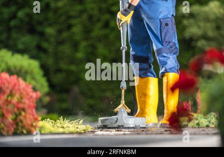 Garden Keeper che lava i mattoni di cemento dal vialetto utilizzando l'idropulitrice Foto Stock