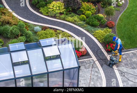 Uomo caucasico nella sua manutenzione degli anni '40 all'interno del suo bellissimo giardino sul cortile. Lavaggio a pressione. Foto Stock