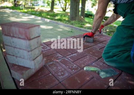 Un esperto lavoratore di pavimentazione si inginocchia durante la posa di pietre di pavimentazione. Foto Stock