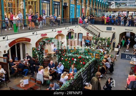 I commensali mangiano ai tavoli sommersi dei ristoranti nell'area sotterranea del mercato di Apple al Covent Garden nel West End di Londra, WC2 nel theaterland Foto Stock