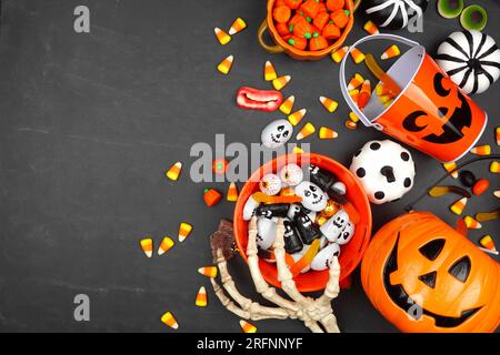 Scherzi di Halloween o delizia il bordo laterale con secchi di jack o lanterna e caramelle assortite. Vista dall'alto su sfondo nero con spazio di copia. Foto Stock