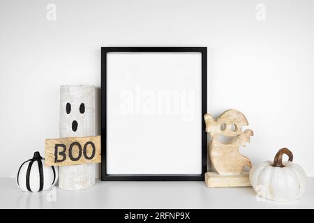 Halloween, un modello. Cornice nera su uno scaffale bianco con decorazioni fantasma in legno rustico e zucche. Cornice verticale contro una parete bianca. Copia spazio. Foto Stock