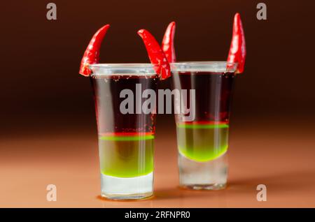 Shot di bevanda a strati preparato con vodka, liquore verde, granadina e succo di limone decorato con peperoncini a forma di corna, shot di diavolo Foto Stock