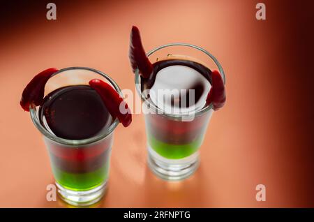 Shot di bevanda a strati preparato con vodka, liquore verde, granadina e succo di limone decorato con peperoncini a forma di corna, shot di diavolo Foto Stock