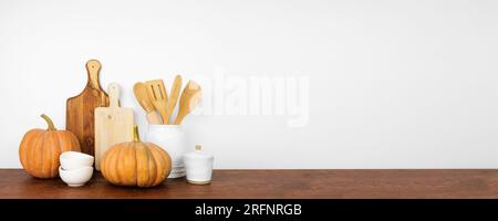 Stoviglie e utensili a tema autunnale con zucche rustiche su una mensola o un bancone in legno. Striscione su sfondo bianco con spazio per la copia. Autunno Foto Stock