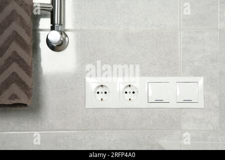 Interruttori delle luci e prese di corrente sulla parete grigio chiaro del bagno Foto Stock