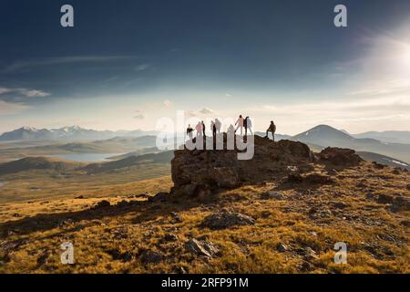 Un grande gruppo variegato di sagome di escursionisti si erge in cima alla montagna e guarda il tramonto Foto Stock