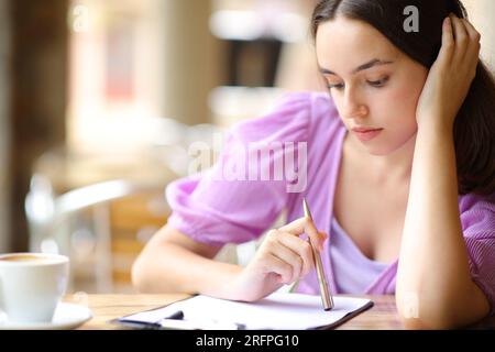 Donna che pensa prima di compilare il modulo in una terrazza del bar Foto Stock