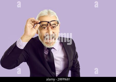 Ritratto dell'allegro uomo d'affari anziano in abito e occhiali sullo sfondo lilla dello studio Foto Stock