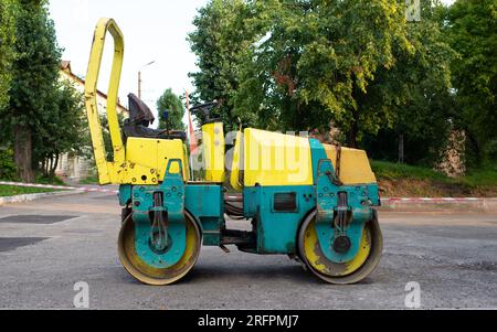 Rullo di vapore in piedi su un percorso con un vecchio muro di pietra e alberi sul retro. ristrutturazione stradale, riparazione di pavimentazioni Foto Stock