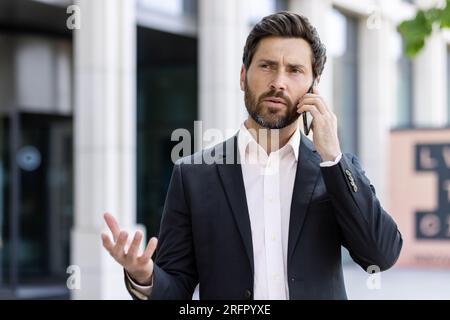 Uomo d'affari preoccupato e serio, in completo accordo e parlando in modo esplicito al telefono, risolvendo problemi e domande. Foto Stock
