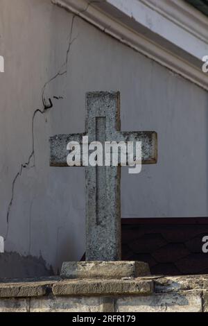 Una lapide con il simbolo del dollaro a tre linee IHS contro un vecchio muro di pietra con una crescita eccessiva in primo piano. Foto Stock