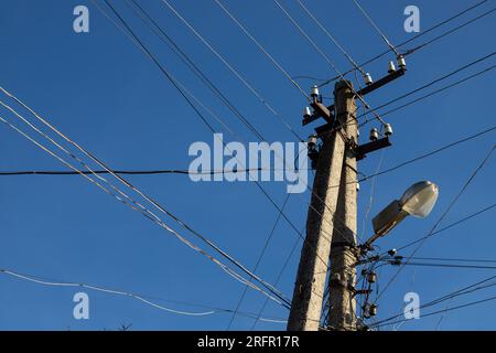 Fili elettrici appesi su un palo con una lampada di illuminazione fotografata dal basso su uno sfondo di cielo blu. Foto Stock