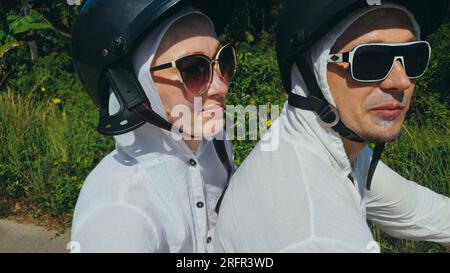 Due donne turistiche caucasiche guida uomo su scooter rosso. Fai selfie. Coppia d'amore in moto in abiti bianchi per andare sulla foresta strada percorso viaggio. Motocicletta affitto casco di sicurezza occhiali da sole. Giro turistico. Foto Stock