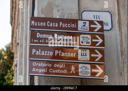 Un cartello marrone con indicazioni turistiche, che mostra le indicazioni per le attrazioni turistiche della città di Lucca nella regione Toscana d'Italia Foto Stock