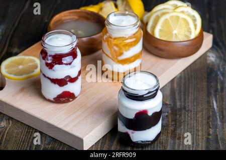 Yogurt a base di latte fresco con aggiunta di marmellata dolce di limone, fragole e mirtilli, confezionato in vasetti di vetro yogurt alla bacche Foto Stock