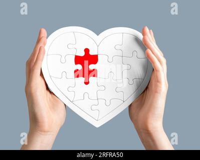 Puzzle a forma di cuore nelle mani isolato su bianco con pezzi rossi. Concetto di problemi d'amore. Foto Stock