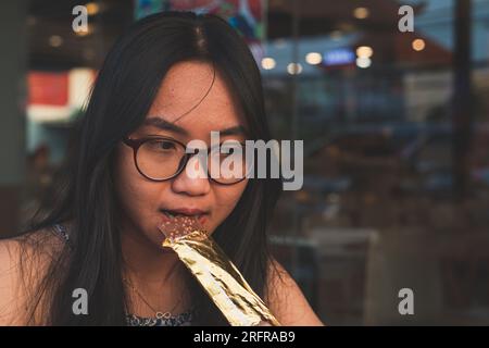 Da vicino la giovane donna felice che morde una barretta di cioccolato. Concetto di cibo per lo stile di vita delle persone Foto Stock