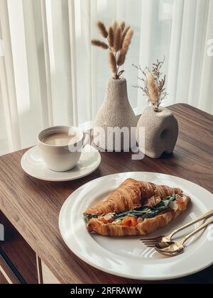 Croissant con salmone e uova strapazzate con caffè su un tavolino Foto Stock