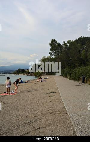 Passeggiata panoramica accanto a una riva del lago delimitata da un parco su un tramonto nuvoloso Foto Stock