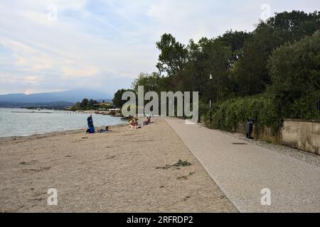 Passeggiata panoramica accanto a una riva del lago delimitata da un parco su un tramonto nuvoloso Foto Stock