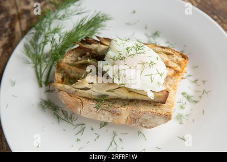 Sgombro affumicato caldo, Scomber scombrus, servito su pane con lievito naturale tostato al burro con uovo in camicia e guarnito con aneto. Inghilterra Regno Unito GB Foto Stock